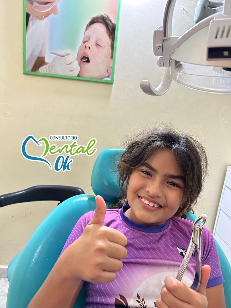 Niña sonriente en el sillón dental de Dental OK haciendo un gesto de aprobación después de la extracción de un diente de leche
